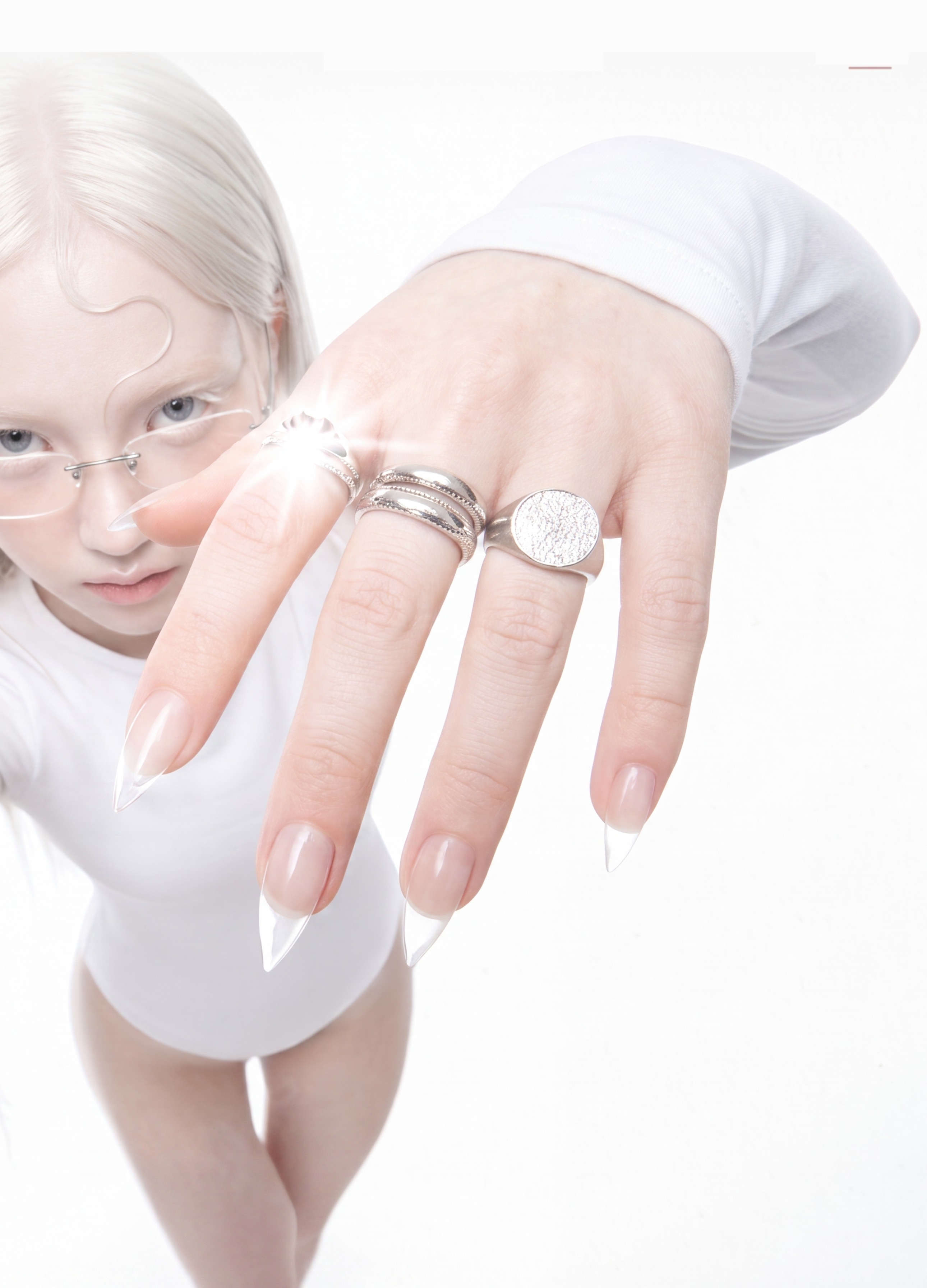 Model in white, wearing silver rings against a bright studio backdrop